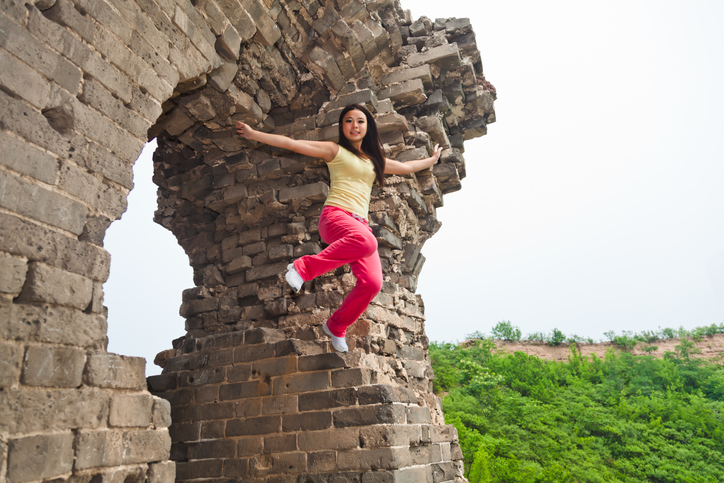 East Asian girl jumping through the Great Wall of China