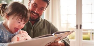 Father With Down Syndrome Daughter Reading Book At Home Together